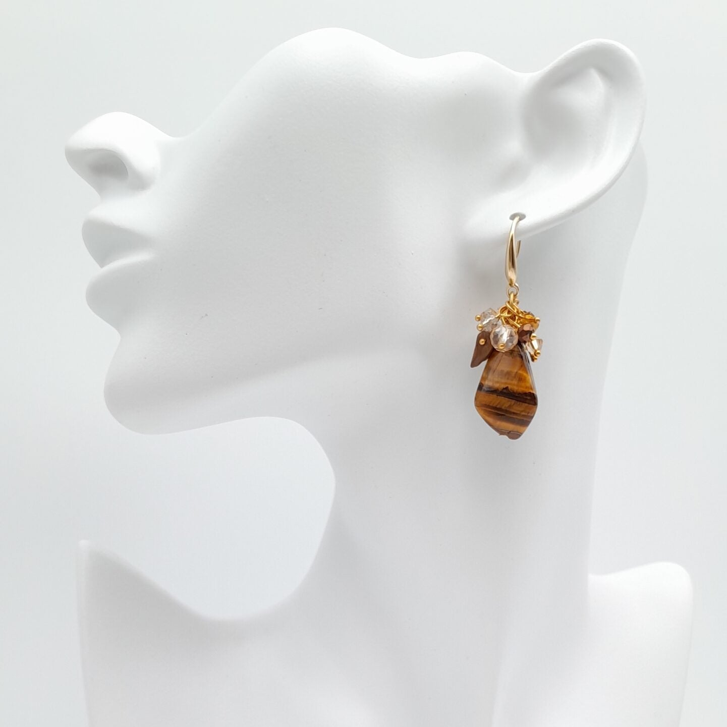 Gold earring with a tiger eye stone on a white bust