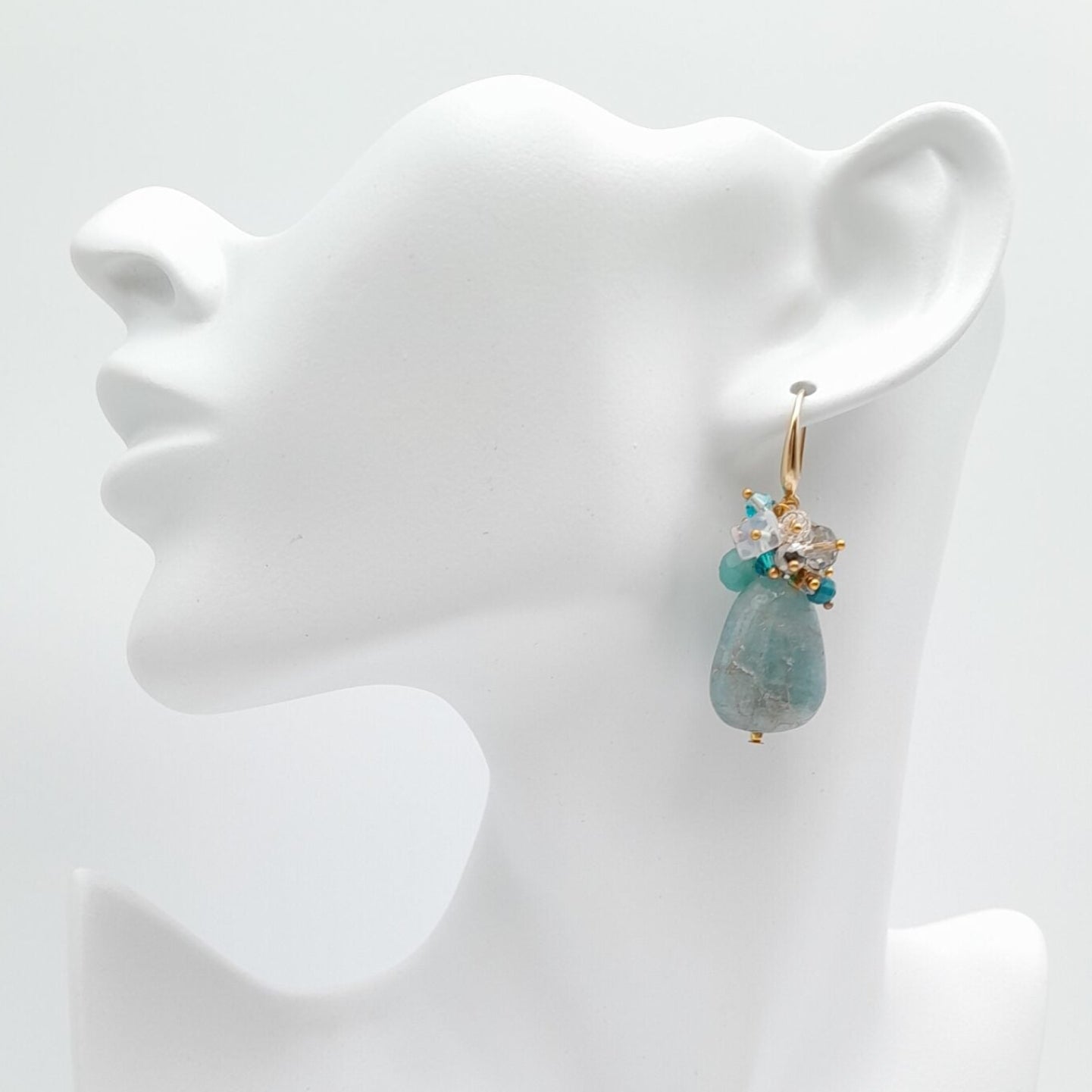 Teal earrings on a white mannequin bust against a white background