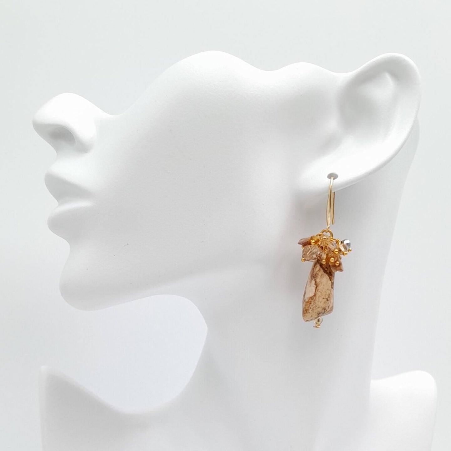 Gold earrings on a white mannequin bust against a white background