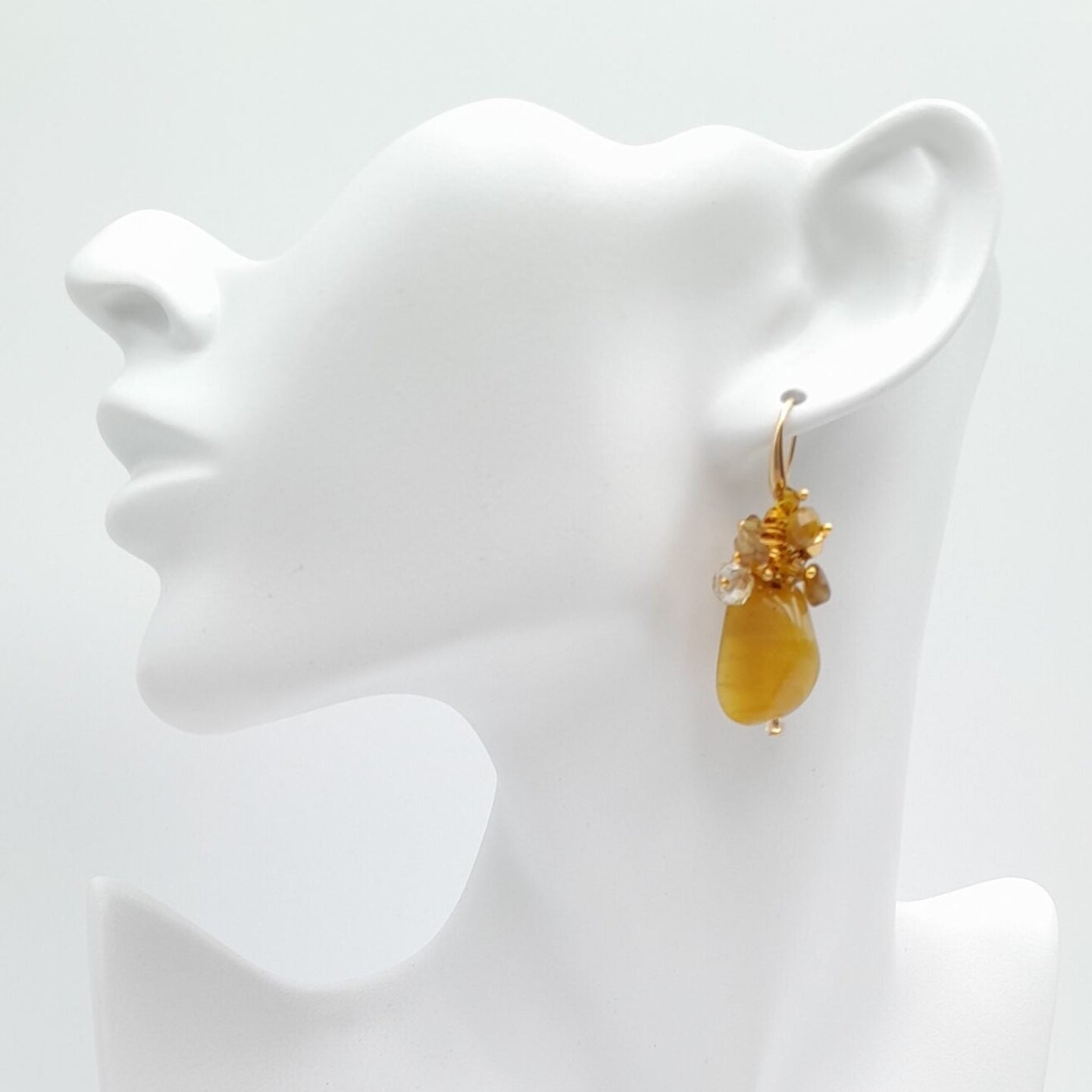 Yellow green earring on a white mannequin bust against a white background